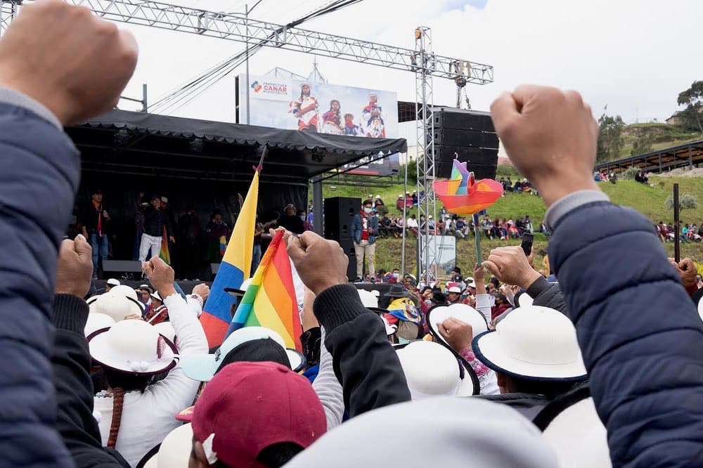 People in varied clothing in front of a stage, facing a single speaker and cheering.